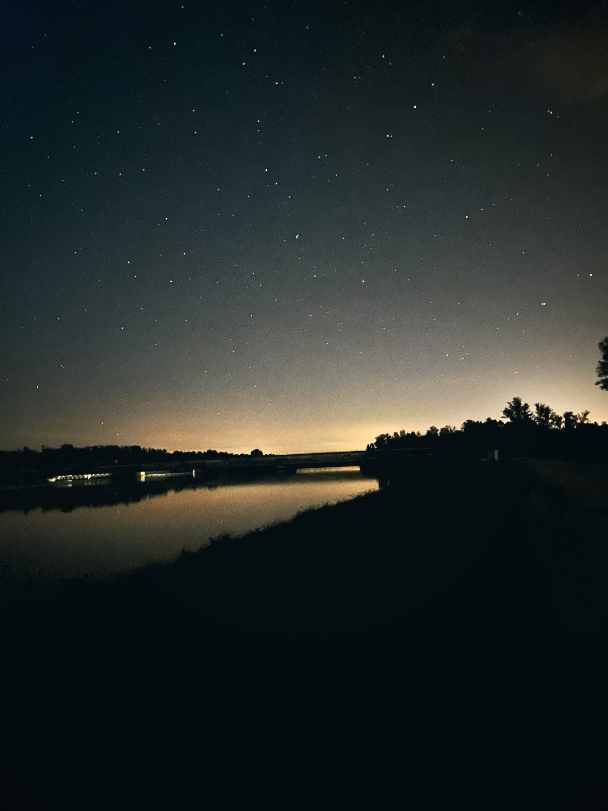 Ein dunkler See unter Sternenhimmel, am Horizont ein heller Streifen