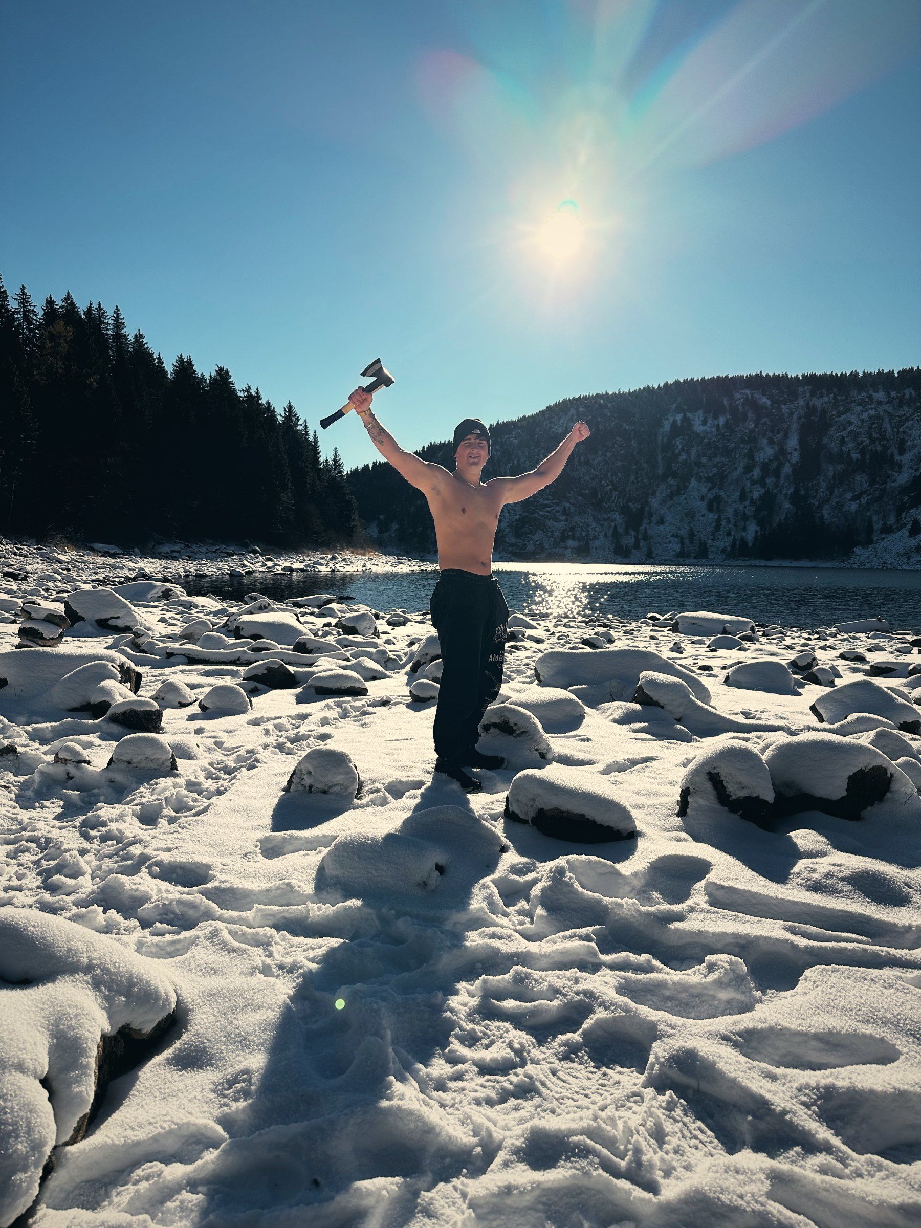 Tea mit Axt in der Wintersonne am verschneiten Ufer