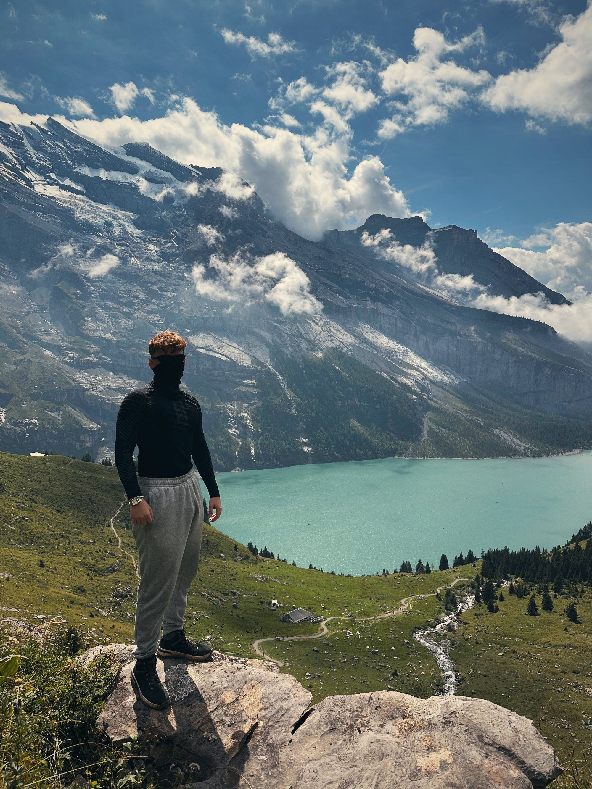 Tea in a face mask on a rock high above turquoise Lake Oeschinen