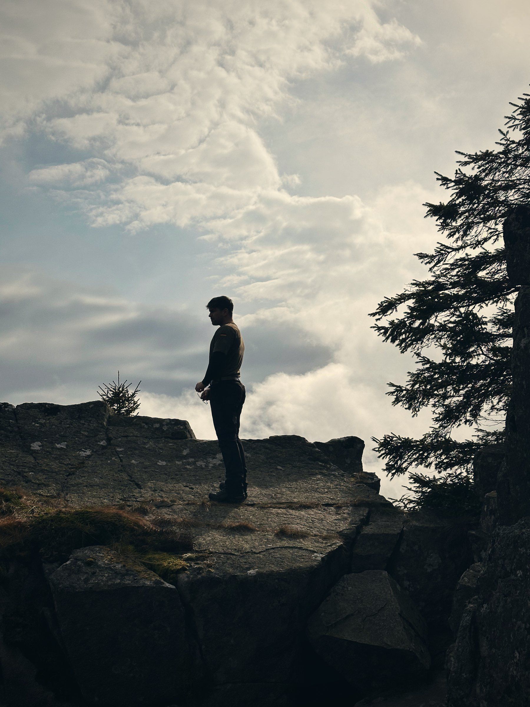 Silhouette auf einer Felskante vor hellen Wolken